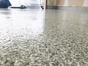 Close-up of a shiny epoxy floor with a speckled pattern, reflecting overhead lights, with cleaning equipment in the background.