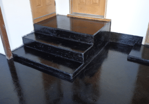 Glossy black epoxy flooring leading up to dark steps and a double wooden door entry, reflecting the surrounding area.