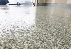 Close-up of a shiny epoxy floor with a speckled pattern, reflecting overhead lights, with cleaning equipment in the background.