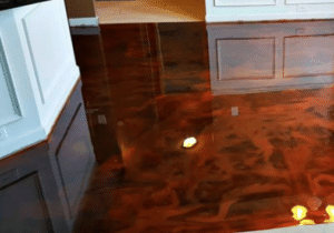 A high-gloss, marbled finish concrete floor in a kitchen with white cabinetry, reflecting the lights and surrounding environment.