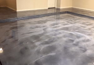 Glossy finished concrete floor inside a room with beige walls, reflecting overhead lights and a door in the background.